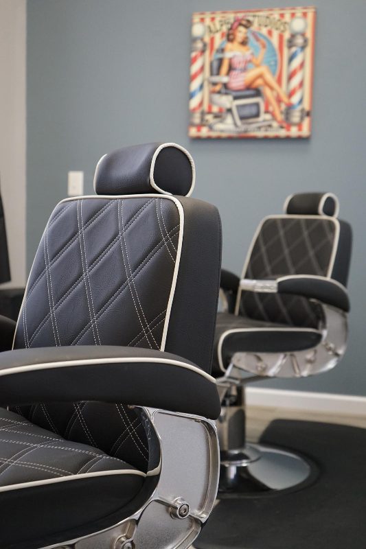 Two black and white barber chairs facing the Alpha Studios pin-up sign